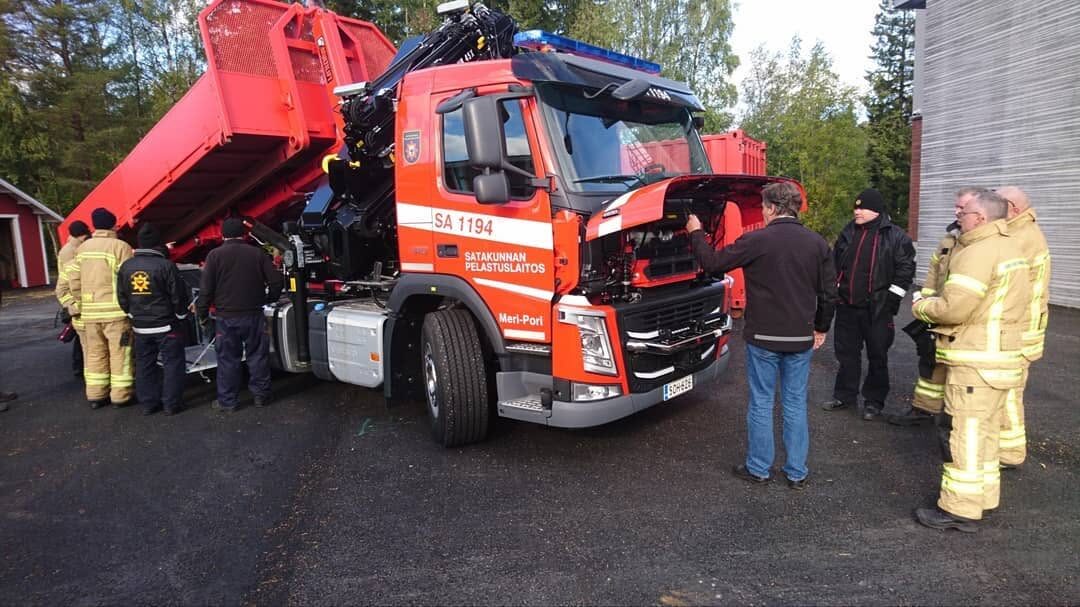 Ryhmä ihmisiä, osa pelastajan varusteissa, tutustumassa kuorma-auton nosturiin ja ohjaamoon.